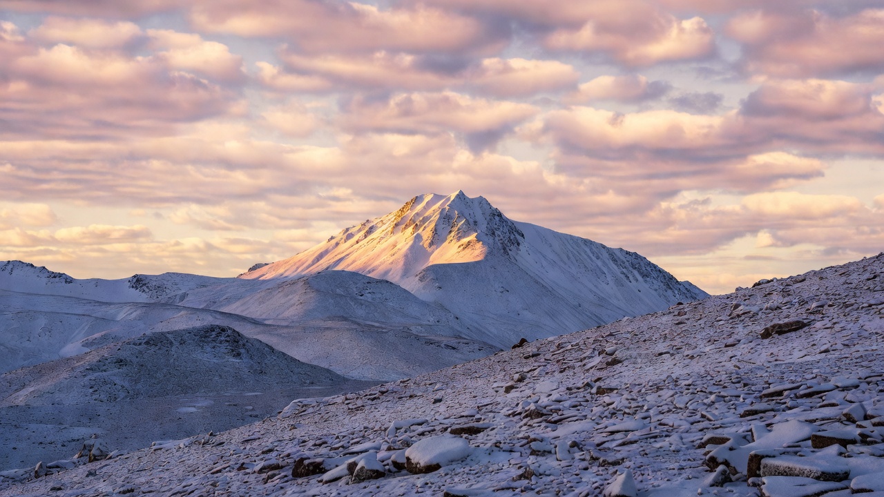 清晨雪山主峰与前景覆雪碎石坡的横向风景照，天空布满高积云，冷蓝与暖橙色调交融
